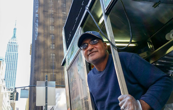 Mahmoud Selin stands at the back of his Halal cart, the Empire State Building visible in the background