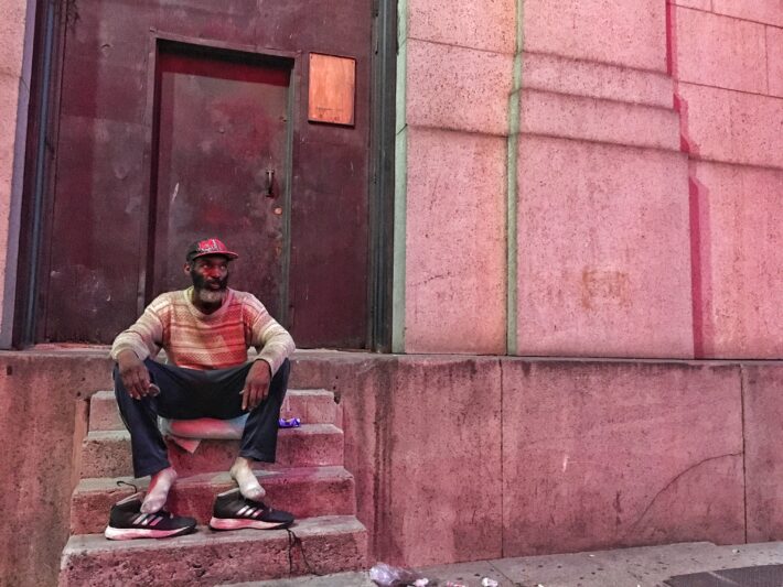 Robert White, who is homeless, sits in the iridescent glow of Madison Square Garden, across the street. Photo: Alex Mierjeski. 