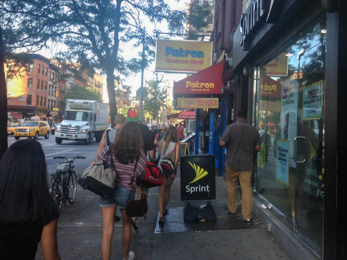 People walk down Ninth Ave. in Hell's Kitchen, maneuvering around sidewalk advertisement signs in front of businesses such as Sprint and Patron Mexican Grill. Photo: Stassy Olmos